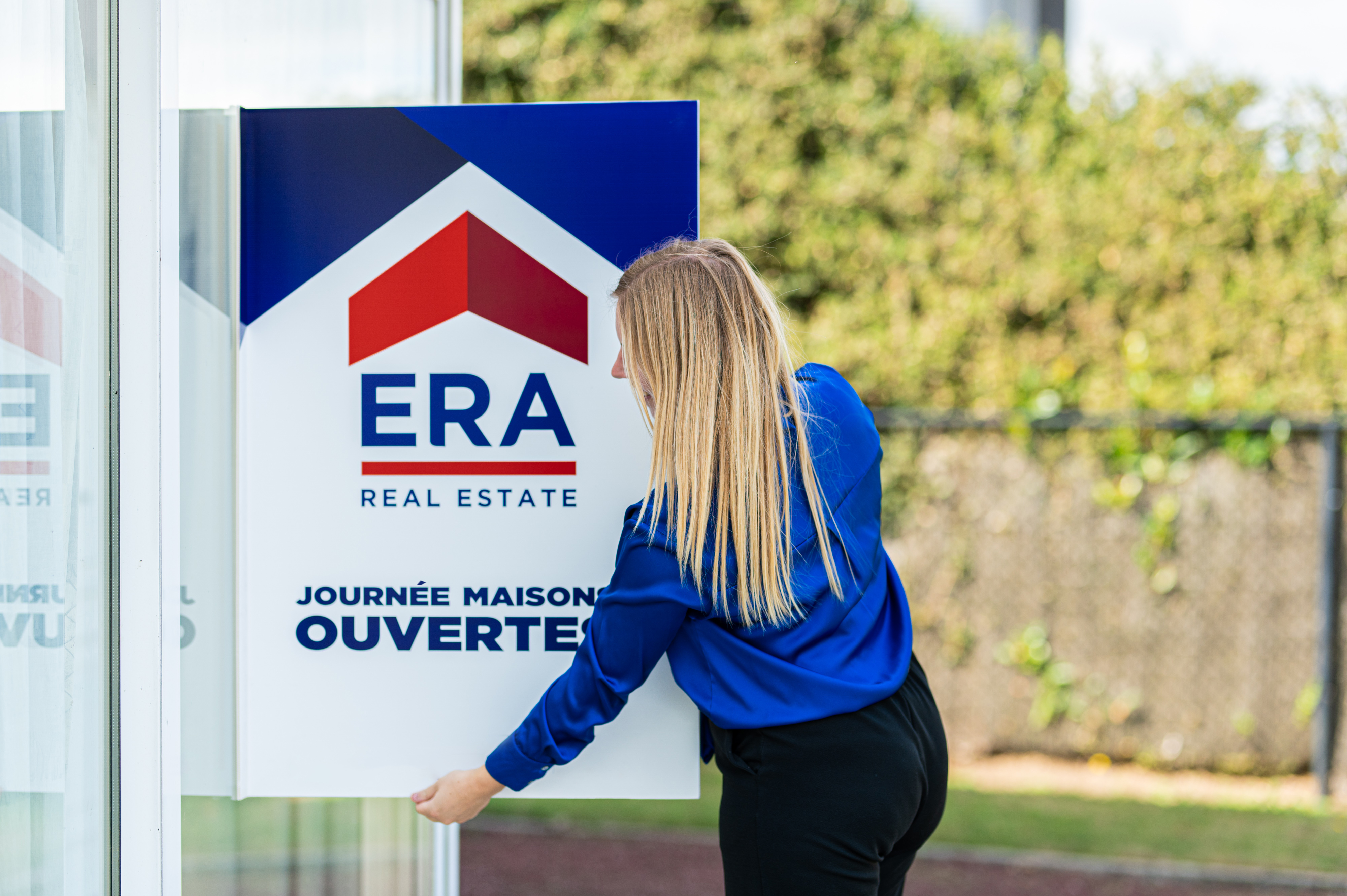 Un agent immobilier ERA place un panneau en V de la Journée Maisons Ouvertes.