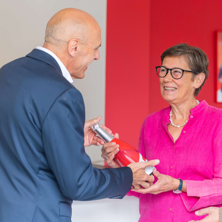 Een ouder koppel krijgt een ERA cava-fles overhandigd door een ERA makelaar, na aankoop van hun nieuwe woning.