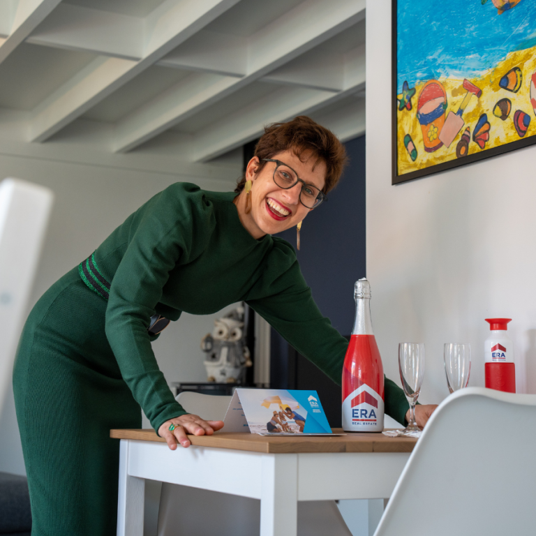 Een lachend makelaar in een pand met een ERA fles, twee champagne glazen en een ERA dopper.