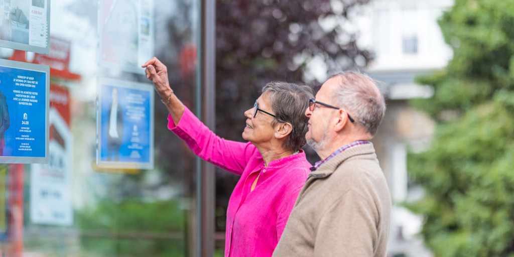 Twee potentiële kopers kijken naar de etalage fiches van een ERA kantoor.