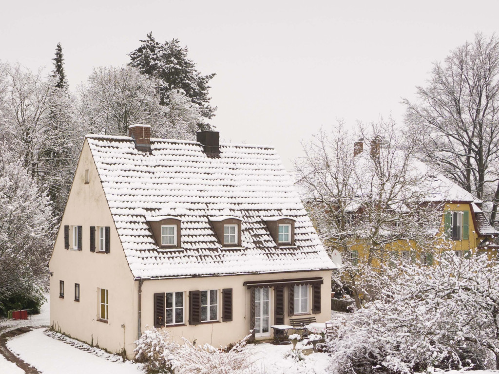Een huis in de winter, met sneeuw op het dak en in de tuin.