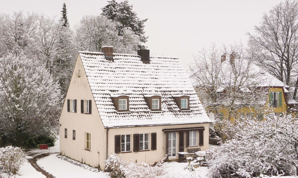 Een huis in de winter, met sneeuw op het dak en in de tuin.