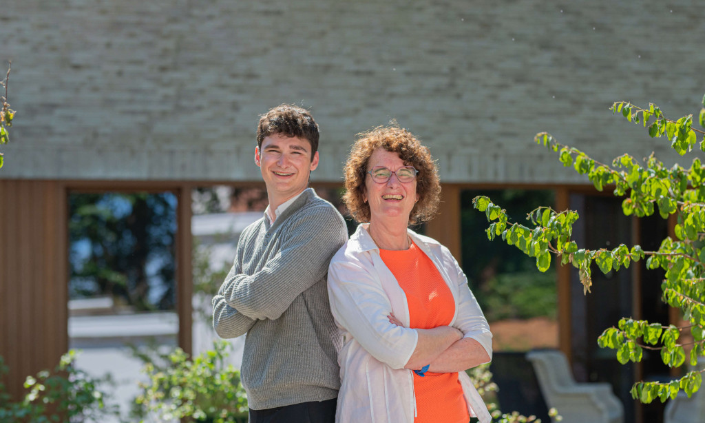 Topmakelaars Dorine en Matthew lachen naar de camera terwijl ze rug tegen rug in de zon staan.
